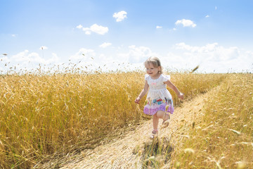 Happy two years old girl running on farm rye field road outdoors at summer