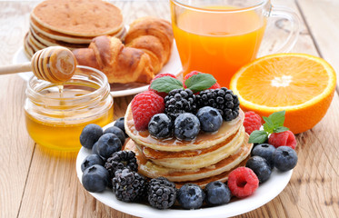 Healthy Breakfast.Pancakes with berries,fresh juice, croissants and honey.