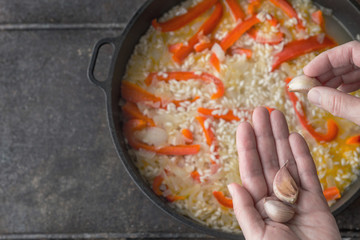 Adding garlic in the pan with rice and bell pepper top view