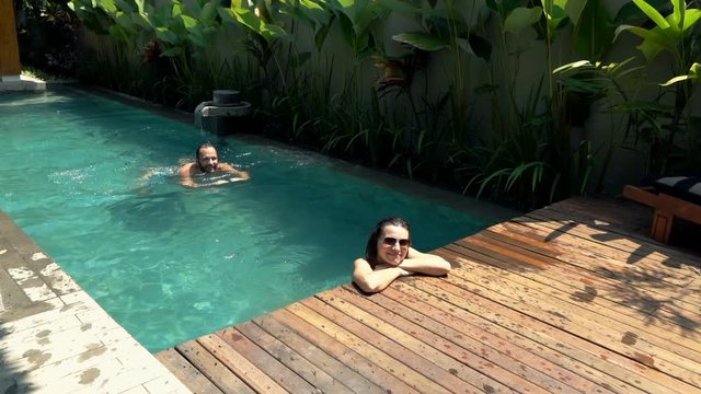 Portrait of happy, young couple relaxing in swimming pool, super slow motion 120fps
