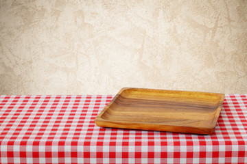 Empty wooden tray on red tablecloth over cement wall background