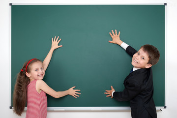 school boy and girl put hands on blank chalkboard and make frame, education concept