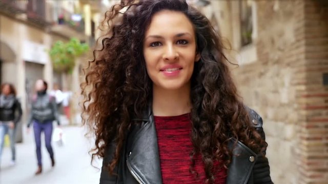 Portrait of happy young woman with beautiful curly hair walking in the city, slow motion