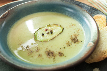 Vegetable green soup-puree with vegetable marrow and bread in clay bowl. Closeup of healthy vegetarian food 