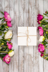 Beautiful flowers peonies with gift box on light wooden background. Top view.
