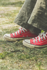 Woman's legs in green summer pants and red canvas sneakers, sitting in a park.