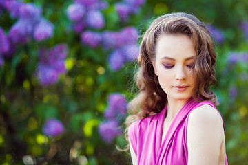 Fototapeta premium Young beautiful girl posing near lilac bushes in blossom