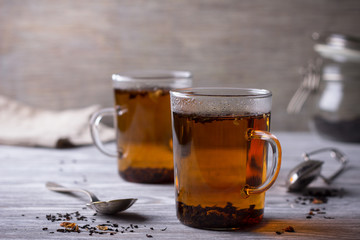 Freshly brewed black tea with rose petals on the wooden table, selective focus