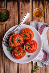 Baked stuffed chicken tomatoes in white bowl on wooden background. Selective focus
