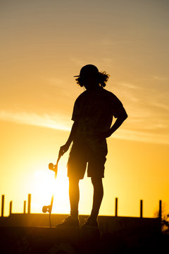 Teen boy silhouette with skateboard at sunset