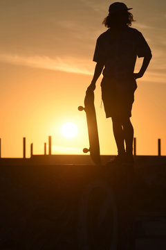 Teenager boy silhouette with skate board at sunset