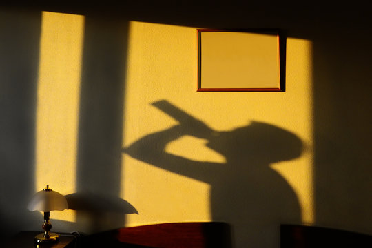 shadow of the alcoholic drinking from a bottle on a yellow wall