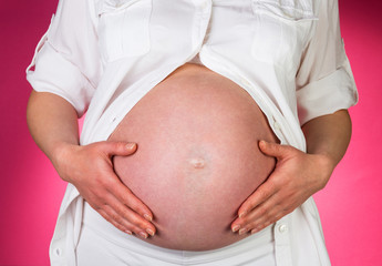 Pregnant woman is stroking belly with hands on  pink background.