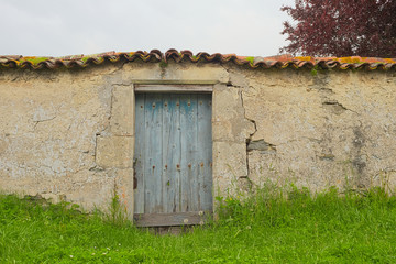 Hintergrund – Mauer mit blauer Tür und Dachziegelabdeckung und grüner Wiese