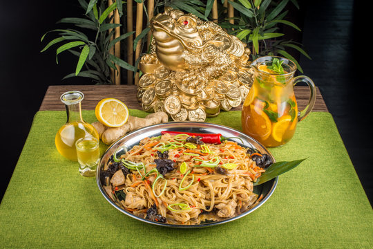 Asian cuisine, noodles with mushrooms, herbs and chili peppers on a background of money frog
