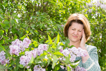 Woman suffering from migraine about blooming lilac