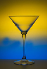 A glass of martini,is not filled, on colored blue-yellow background.