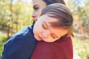 Mother holding kid boy sleeping in her shoulder