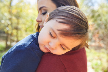 Mother holding kid boy sleeping in her shoulder