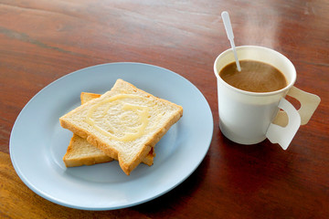 Hot coffee and bread toast topped with milk for breakfast on wood table
