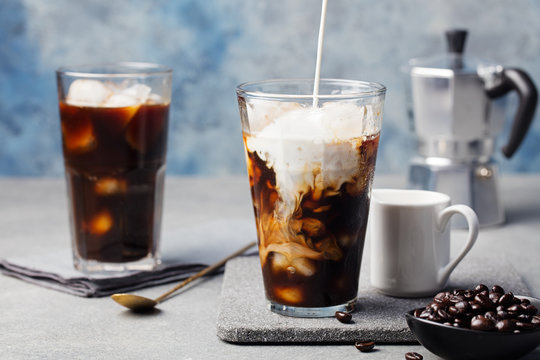 Ice coffee in a tall glass with cream poured over and coffee beans