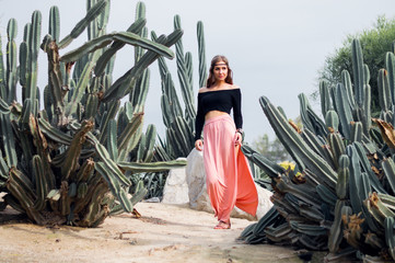 Hippie woman in long pink skirt walking near big cactuses - 111434759