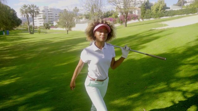 Young woman golfer striding across the fairway with a golf club in her hand as she follows up on her stroke