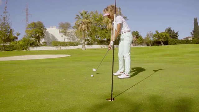 Young woman golfer preparing to sink her putt lining up the ball with the flagg as she enjoys a round of golf