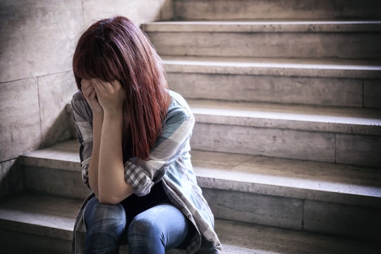 Depressed girl. Adolescent crisis sitting on the steps of a basement, covers her face with her hands.