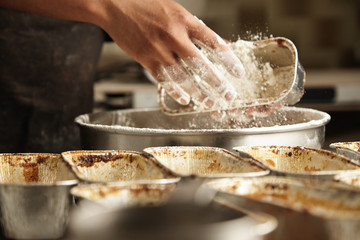 Close focus on hand throws flour inside cake mold, preparation process of professional baking in artisan confectionery with black man chief