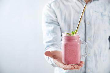 Man offers on camera rustic jar with cold fresh berry smoothie with golden straw and mint leaves...
