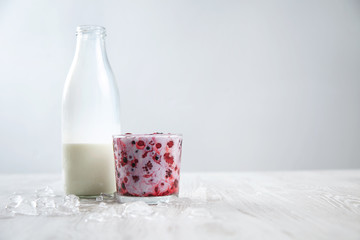 Mixed frozen berries in rox glass mixed with organic fresh milk near vintage bottle isolated on white surrounded with melted ice cubes