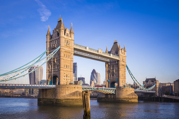 Fototapety  Londyn, Anglia – słynny most Tower Bridge w porannym słońcu z czerwonym autobusem piętrowym i dzielnicą bankową w tle