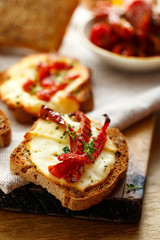 Grilled homemade bread with sheep milk cheese and sun-dried tomatoes on a rustic wooden board