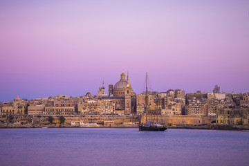 City of Valletta at sunset with St.Paul's Cathedral and sailboat and purple sky, Malta
