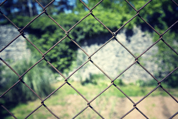 Outside old and rusty iron fence closeup with sunny blurred garden background. Conceptual photo.