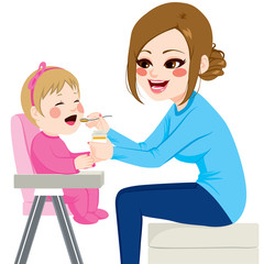 Mother feeding baby with spoon sitting on chair