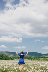 Young beautiful woman in a blue dress enjoying chamomile field among mountains. Summer mood