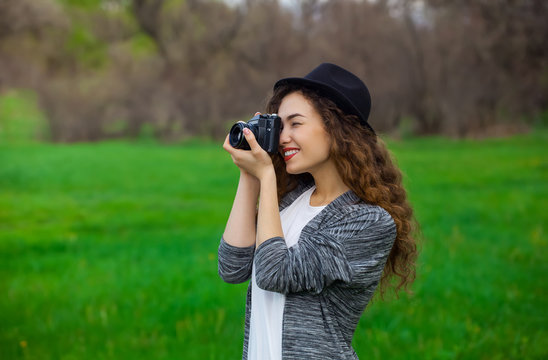 Young, beautiful, smiling girl in a hat and with long, curly hair pictures of the nature in the park film, SLR camera.