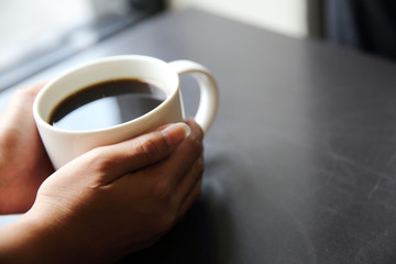 Black coffee with hand on wood background in coffee shop