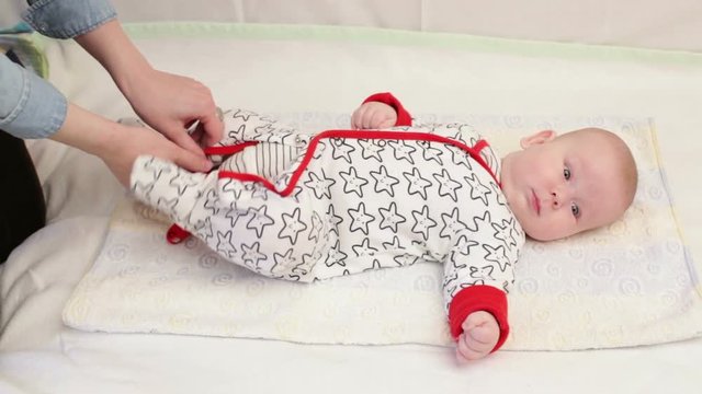 Close up cute little baby is laying on the towel, mother is taking his diaper off