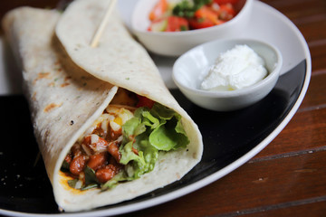 Mexican burritos on a plate with tomato salad