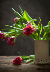 A bunch of fresh pink tulips flowers in a white vase on a white wooden background