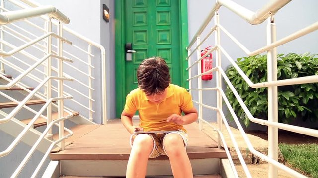 Caucasian young boy sitting on a stairs and using ipad