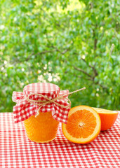 Jar of orange jam and orange halves on a red checkered tablecloth. - 111453114