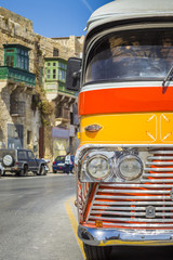 Naklejka na ściany i meble Detail photo of the red and orange coloured iconic Maltese public bus in the Valletta seaside road in Malta