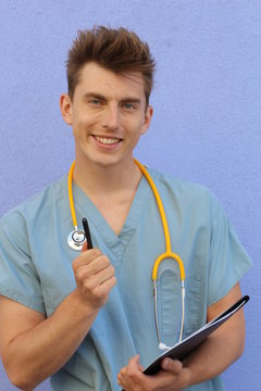 Male doctor pointing at you with pen and holding a notepad or clipboard and wearing medical uniform on blue studio background