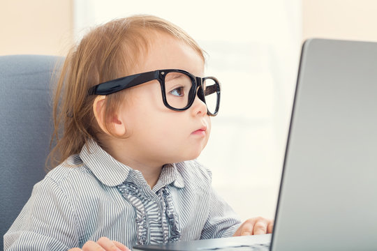 Smart little toddler girl with big glasses on her laptop