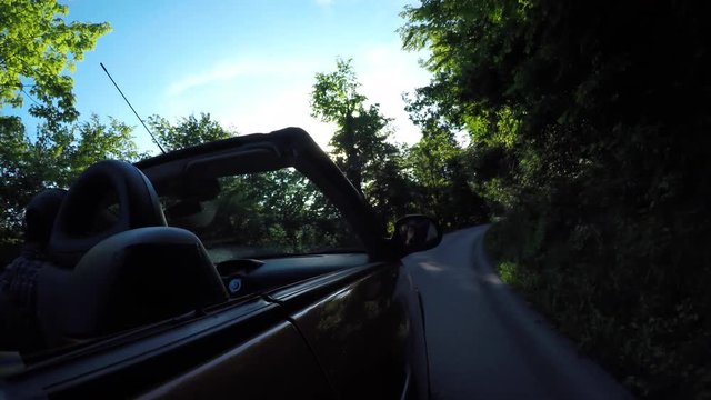 Side shot of a person driving convertible car in country road