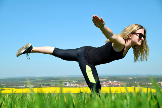 Young woman stretching on a meadow in sunny day.
